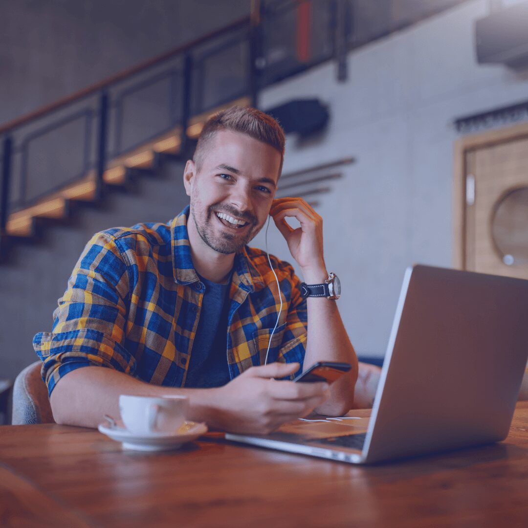 man smiling with earphones in at his laptop
