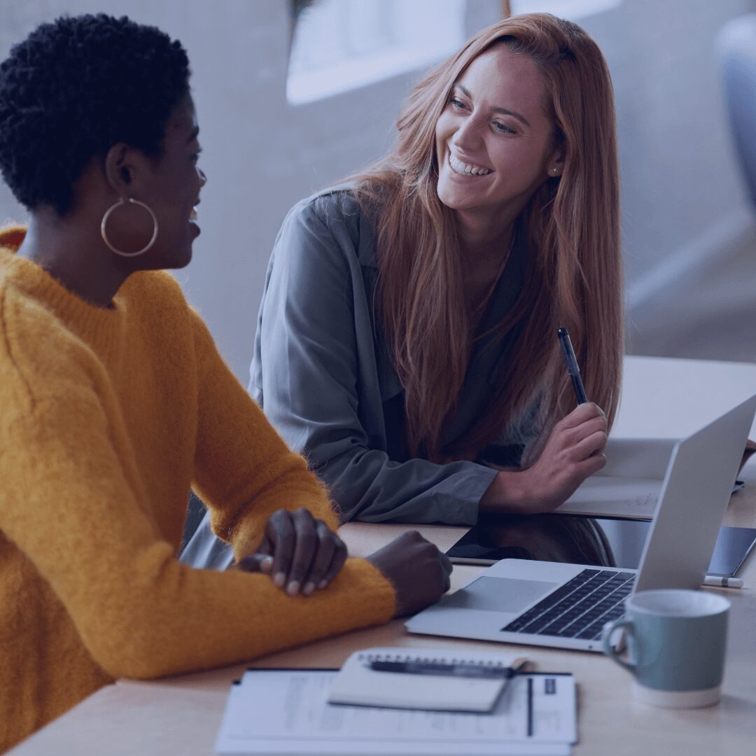 two women talking and smiling while working