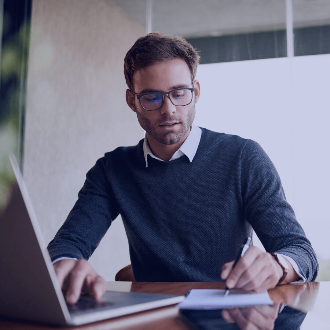 man working at his laptop and writing on notepad